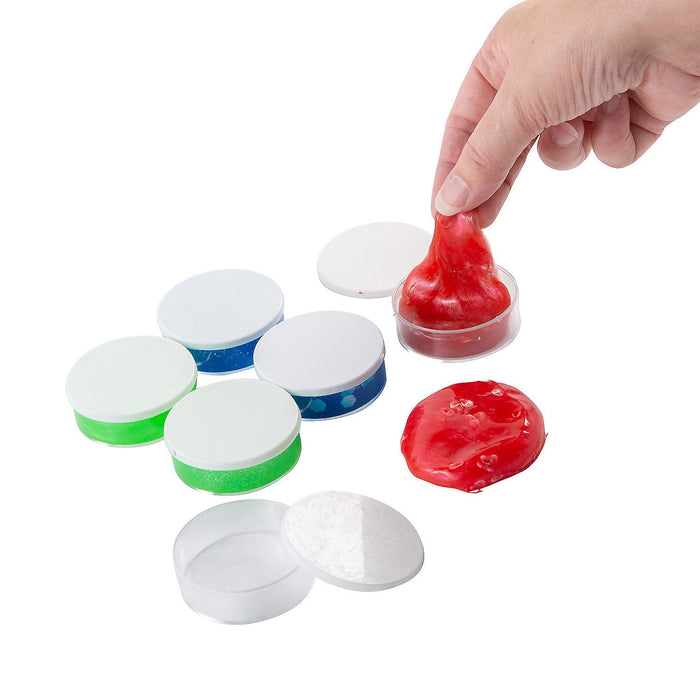 Six continers of slime from the 12 Days of Christmas Slime & Putty Gift Set.  Two green, two blue, and two red.  One red container has the slime removed and on the counter while the other red container is open with a hand stretching some of the slime.