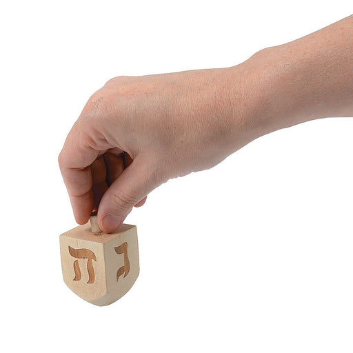 A hand spinning a 2.5 inch tall wooden Dreidel spinning top.