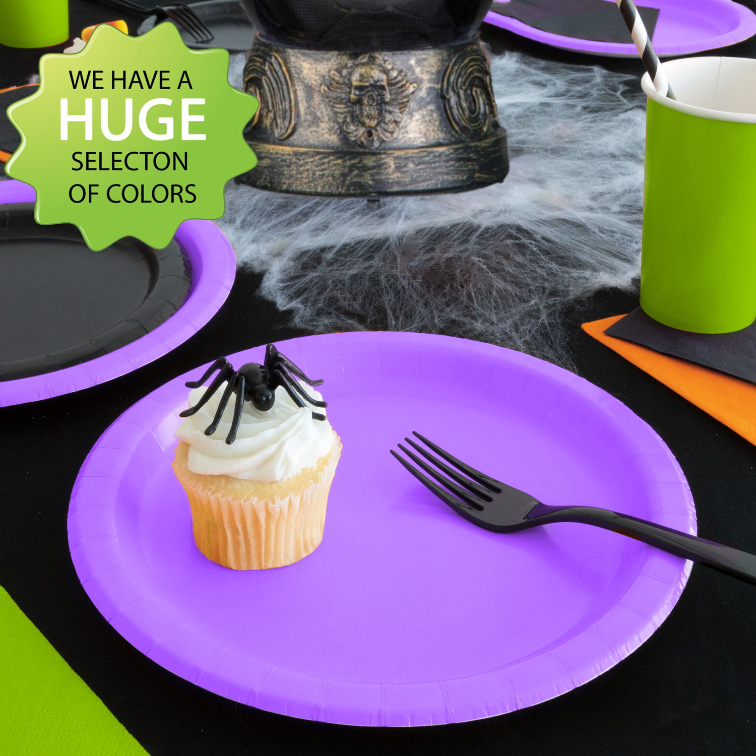 A Halloween themed solid color table setting with spooky decor and tableware in purple, orange, green, and black.