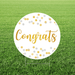 Congrats yard sign featuring a round white sign with gold script “Congrats” lettering and gold and silver confetti dots, displayed in grass.