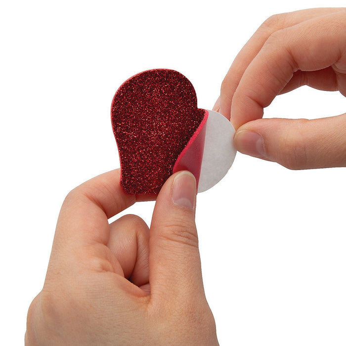 A picture showing someone peeling off the self adhisive backing on a heart from the Dr. Seuss™ The Grinch Growing Heart Ornament Craft Kit Pack.