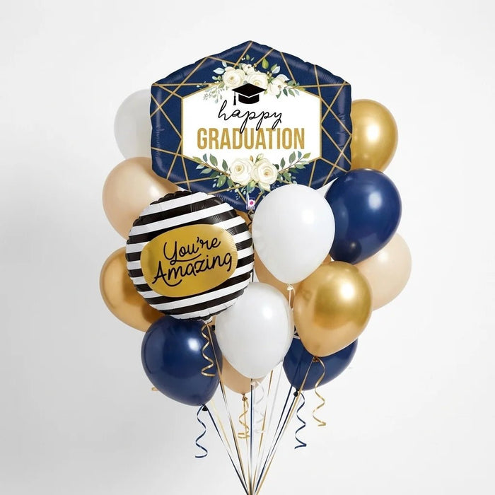 Graduation balloon bouquet featuring a navy and gold “Happy Graduation” foil balloon with white floral accents, a black-and-white striped “You’re Amazing” foil balloon, and navy, white, gold, and ivory latex balloons with curling ribbons.