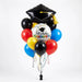 Spanish graduation balloon bouquet featuring a black graduation cap-shaped foil balloon, a round “Felicidades Graduado” foil balloon, and red, yellow, blue, and black latex balloons with curling ribbons.