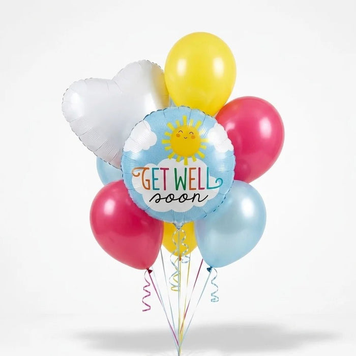 Get well soon balloon bouquet featuring a round blue “Get Well Soon” sun-and-cloud foil balloon, a white heart-shaped foil balloon, and pink, yellow, and light blue latex balloons with curling ribbons.