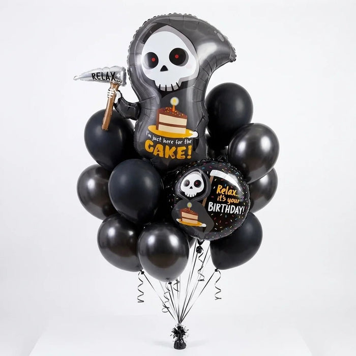 Grim reaper birthday balloon bouquet featuring a large reaper-shaped “I’m just here for the cake!” foil balloon, a round “Relax, it’s your birthday!” foil balloon, and matte black and metallic black latex balloons with curling ribbons.