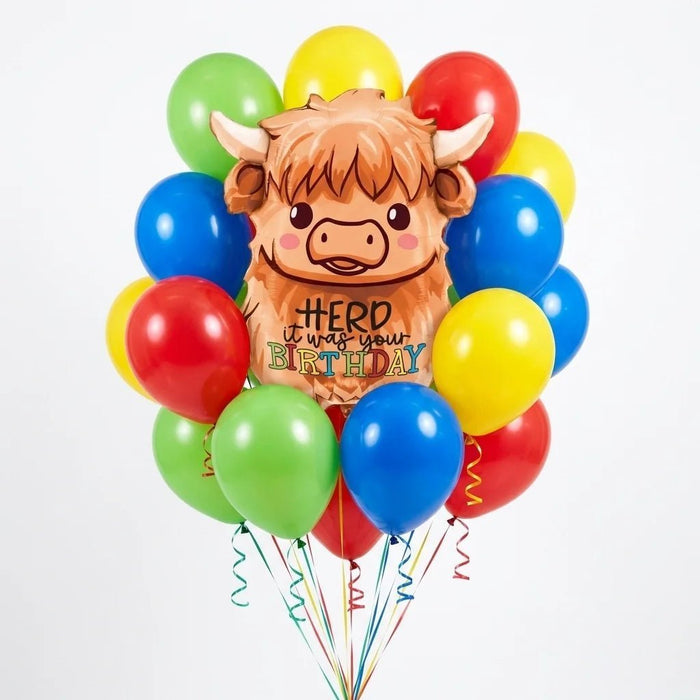 Highland cow birthday balloon bouquet featuring a smiling cow-shaped “Herd It Was Your Birthday” foil balloon and red, yellow, green, and blue latex balloons with curling ribbons.