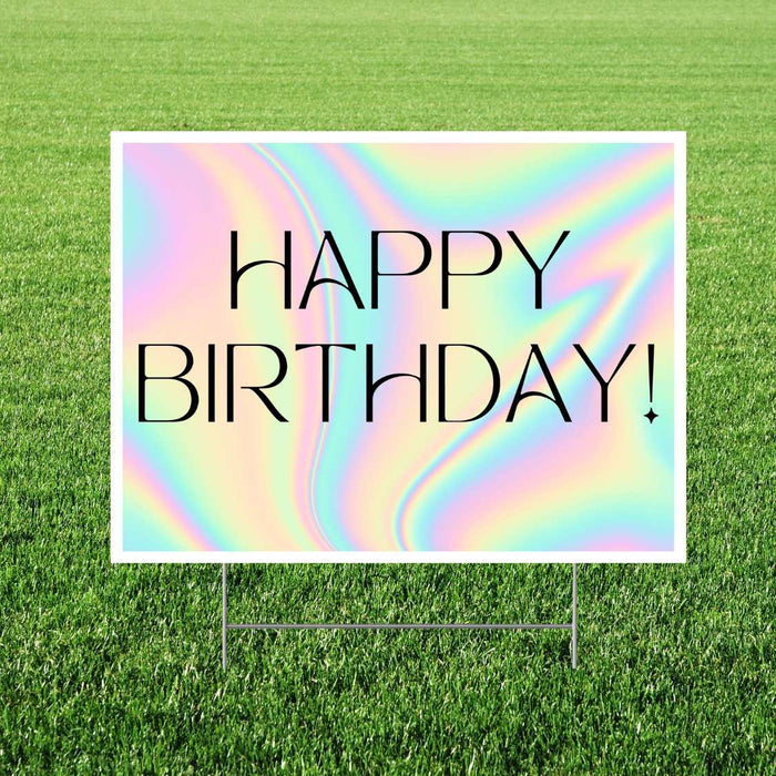 Holographic happy birthday yard sign featuring an iridescent pastel rainbow background, thin black “Happy Birthday!” lettering, and a white rectangular border displayed in grass.