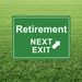 Retirement yard sign designed like a green highway exit sign, featuring white “Retirement” and “Next Exit” text with a white arrow, displayed in grass.