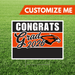 Graduation-themed sign with 'Congrats Grad 2026' on a grass background