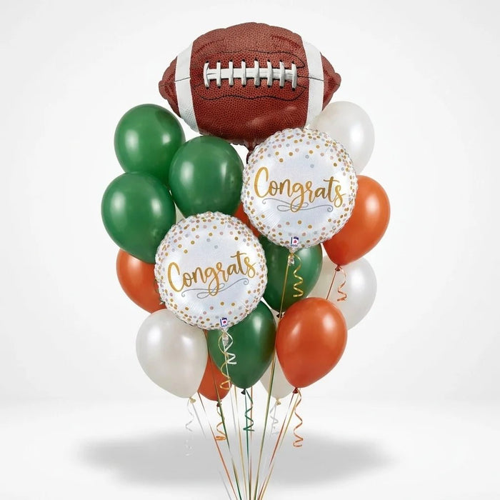 Football congratulations balloon bouquet featuring a large football-shaped foil balloon, two round “Congrats” foil balloons, and green, burnt orange, and white latex balloons with curling ribbons.