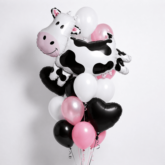 Cow-themed balloon bouquet featuring a large black-and-white cow-shaped foil balloon, black heart-shaped foil balloons, and black, white, and pink latex balloons with curling ribbons.