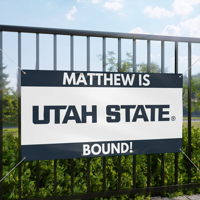Promotional sign for Utah State University with text 'MATTHEW IS UTAH STATE BOUND!' against a natural background.